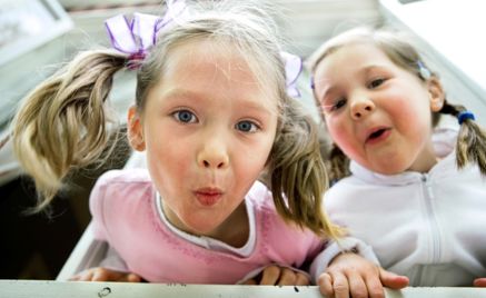 To jenter lener seg ut av vindu. Lager grimaser.