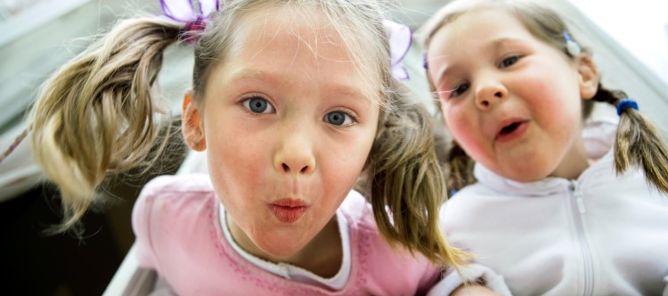 To jenter lener seg ut av vindu. Lager grimaser.